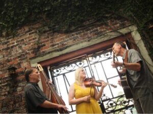 Bill Ellison, Temperance Babcock and Jeff Perkins performing in front of an exposed brick wall with large window.